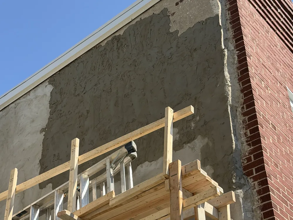 Exterior wall mid-job with scaffolding as new stucco is applied next to brick