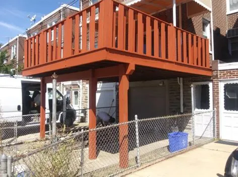 Elevated red-painted deck on posts behind a row home