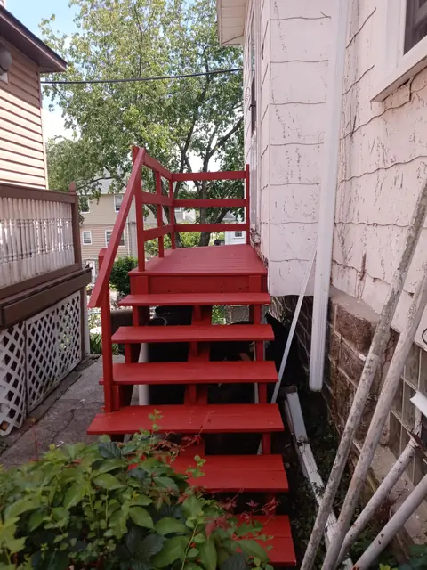 Red-painted exterior wood stairs alongside a house